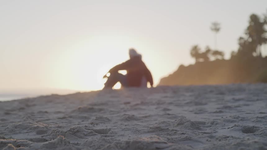 Man sitting on the white sand beach at sunset next to the ocean