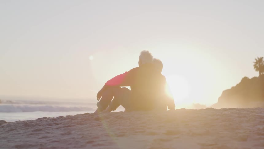 Older couple sitting on the beach watching the waves at the beach