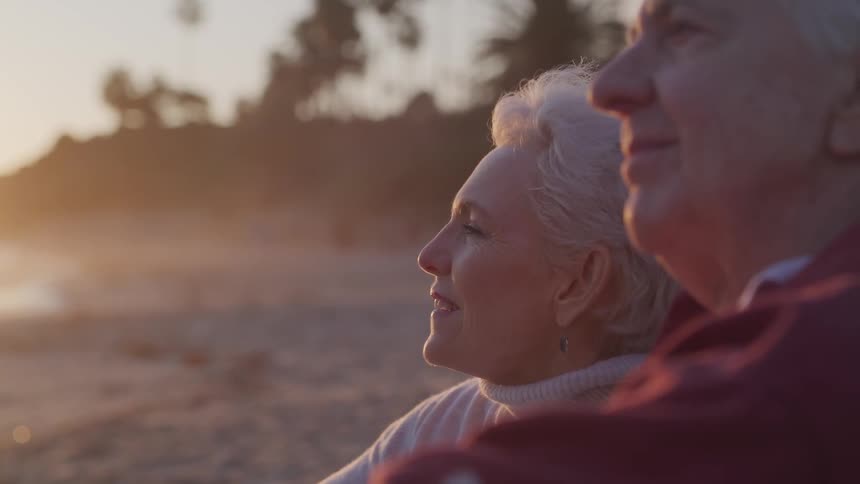 An elderly man and woman are sitting on the beach watching the sun set