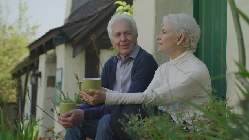 A man and a woman sitting on the porch holding green tea cups and talking
