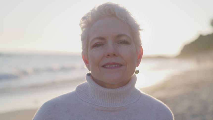 A woman stares into the camera while standing on a beach