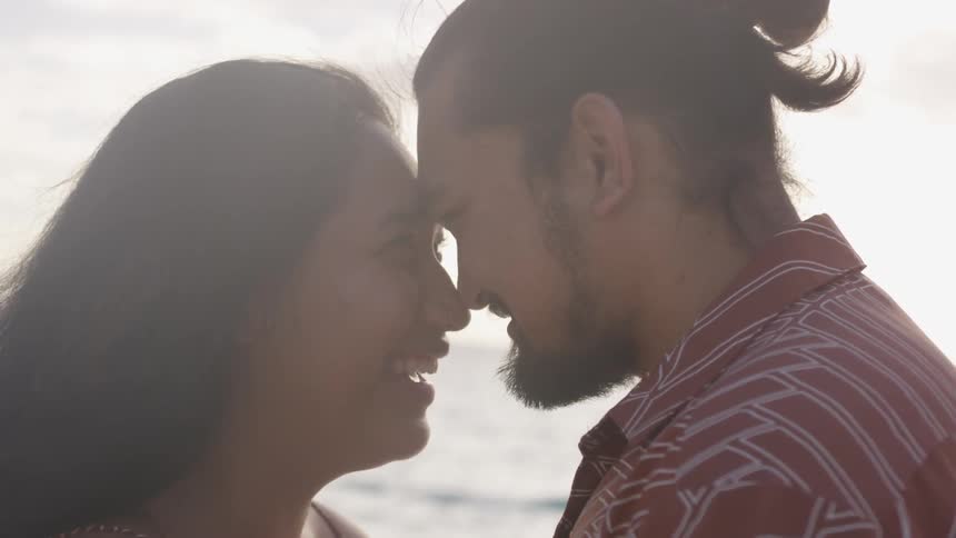 A man and woman stand outside with their foreheads and noses together