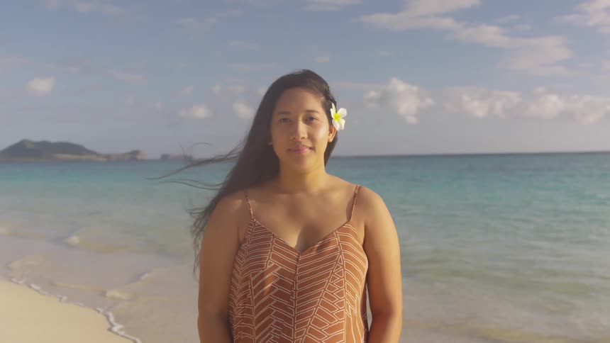 Woman stands on beach near surf wearing flower in her hair