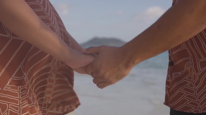 A man and woman are holding hands as they stand on an ocean beach
