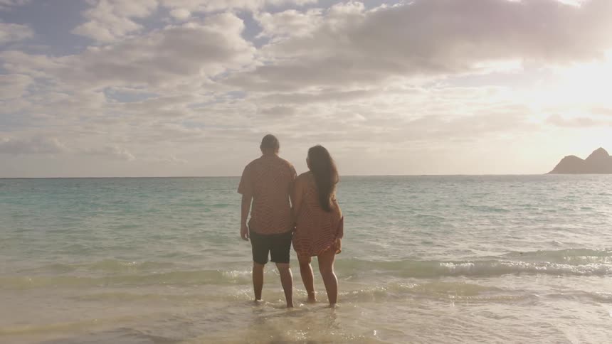 A man and woman hold hands while walking in water on a beach