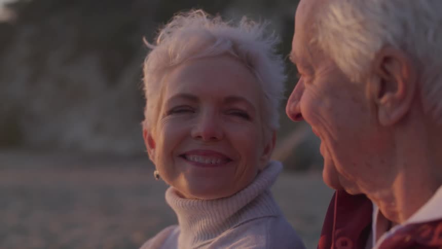 Older couple sitting on the beach and looking lovingly at each other
