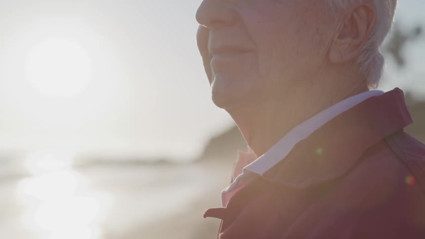 An elderly man looks out over the ocean as he stands on a beach