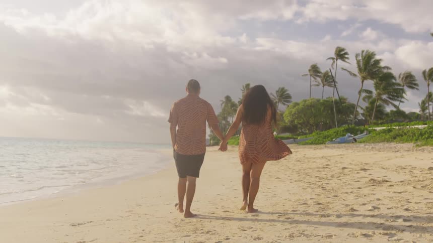 A man and a woman holding hands walking on the beach