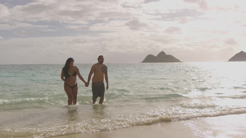 A couple walk out of the surf and onto a beach