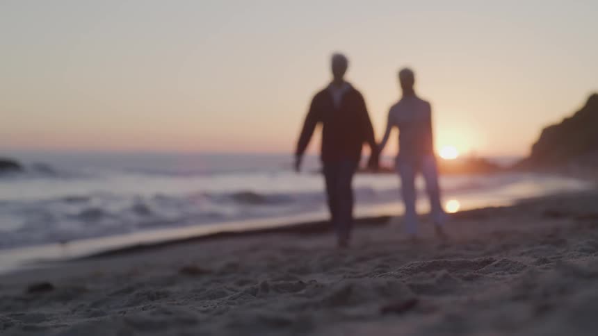 Two people walking on a beach during sunset
