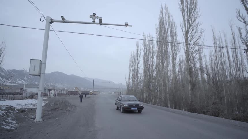 A car passes on a road with a few people walking along on a cloudy day