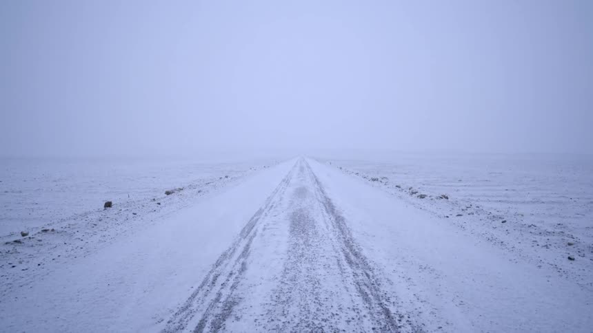 A long and straight road in a snowy and foggy landscape