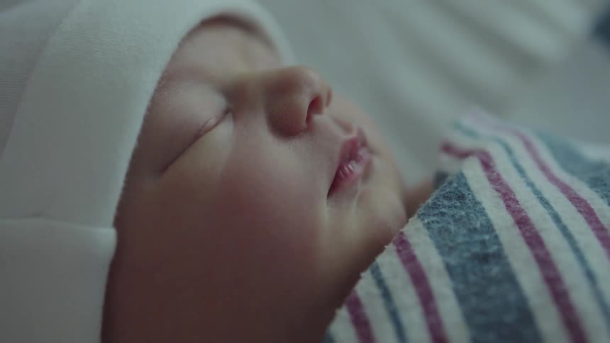 A swaddled baby sleeps while they wear a hat