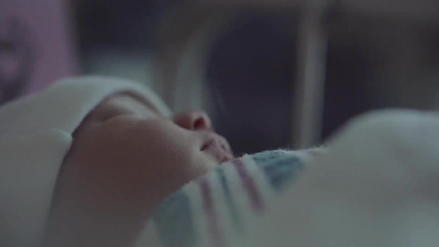 A newborn sleeps while wearing a hat and bundled in a blanket