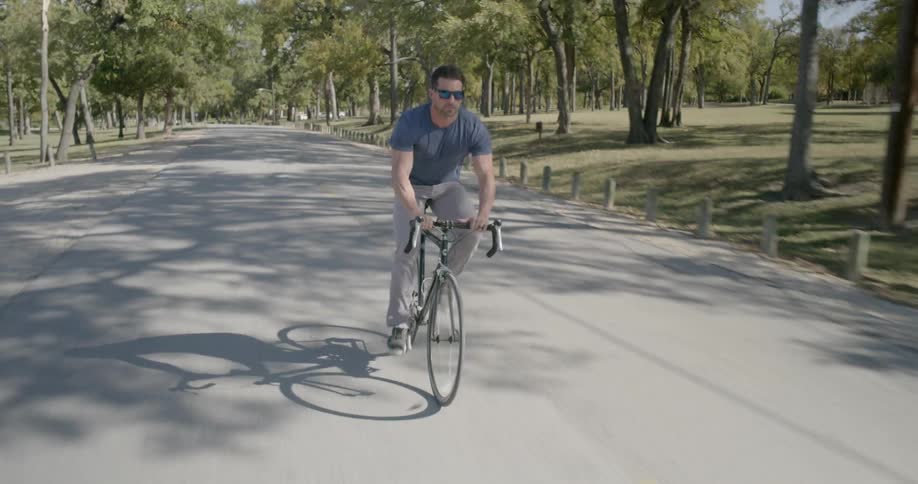 A man cycles down the center of a park road