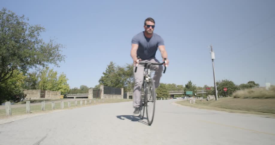 Muscular man wearing sunglasses rides a bike on the road in the countryside