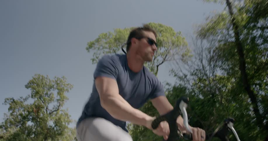 A man wearing sunglasses pedals a bike down the road