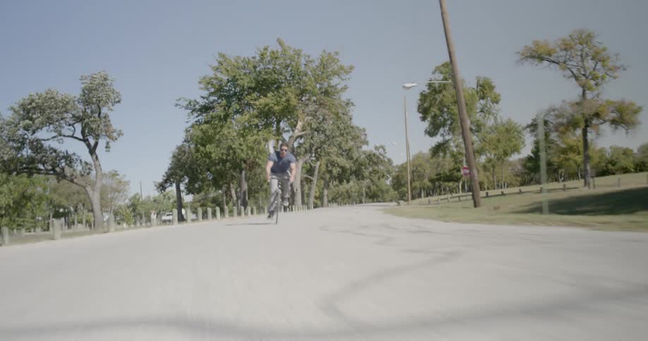 Man rides bike along wide avenue bordered by fields
