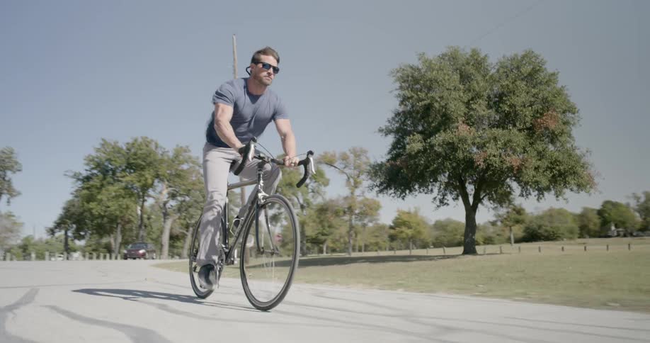 A man rides a bicycle down the street beside a park