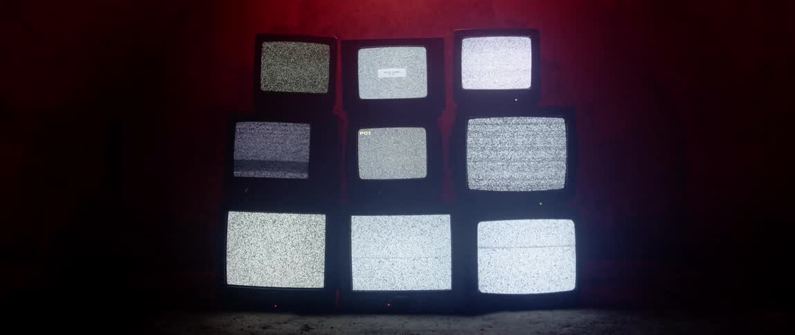 Rows of televisions displaying static stacked atop one another in a dark room