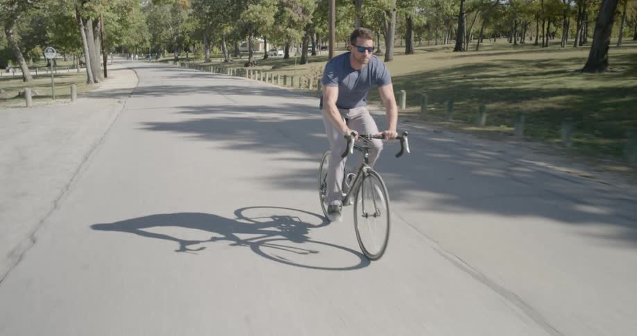 Man rides a bicycle down a road near the park