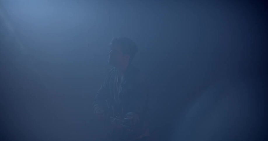 Male singer plays a guitar and sings a song in the spotlight in the dark music studio
