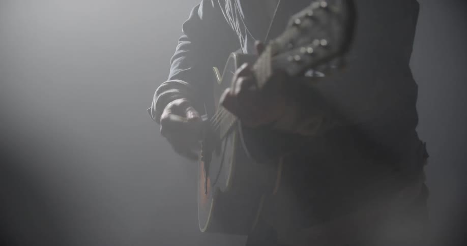 Playing guitarist highlight by sun rays in shadowy hazy room