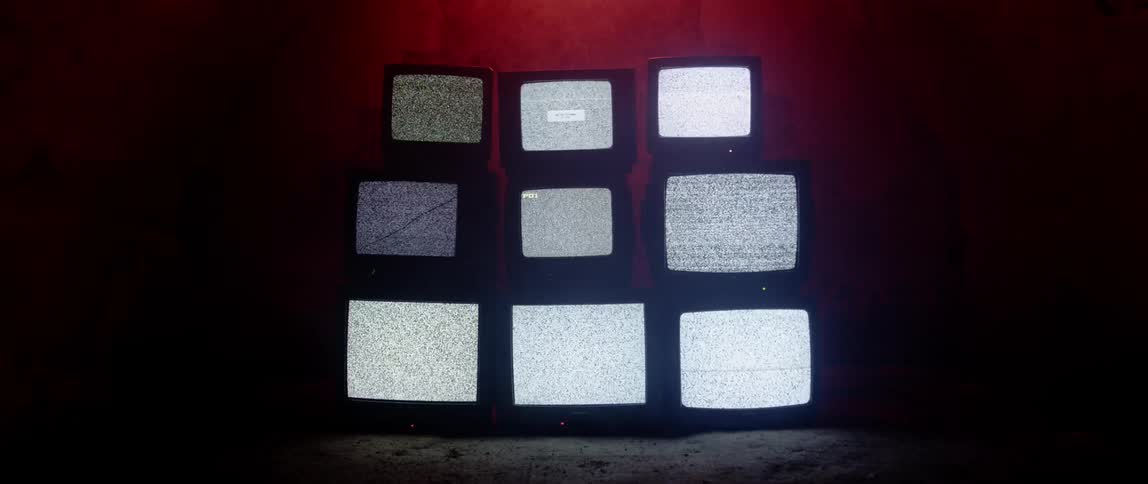 Tube style televisions are stacked upon each other with static playing on the screen