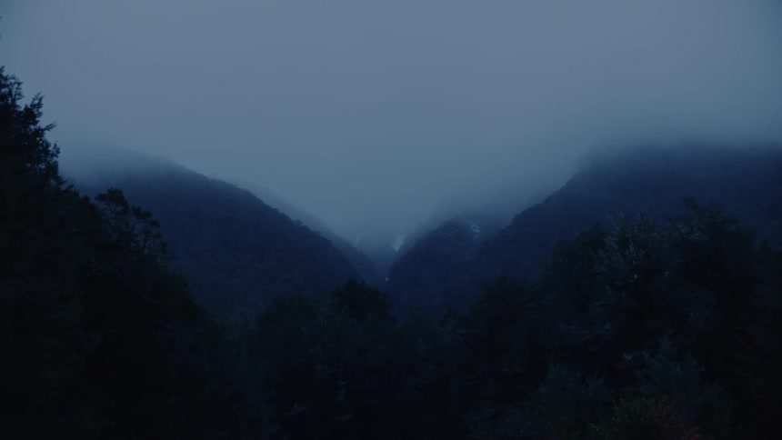 A thick layer fog envelopes mountains that stand out in this darkened landscape