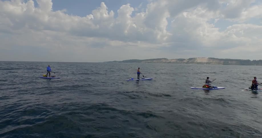 People on paddle boards in a row following a boat in the ocean