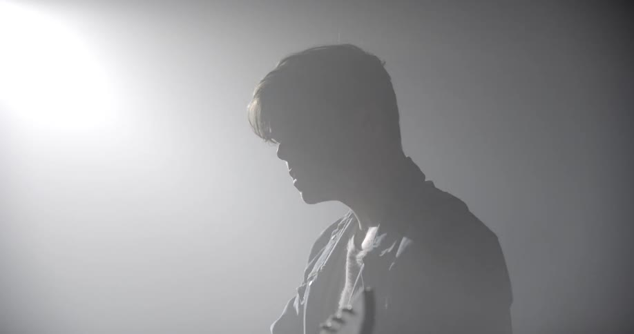 A man plays a guitar as he stands under a spotlight in the dark