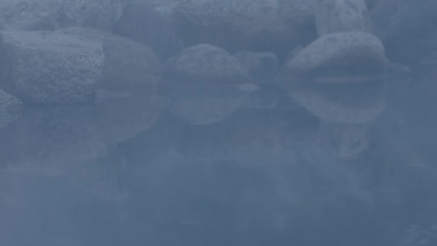 Rocks reflecting in the calm waters of a steamy hot spring