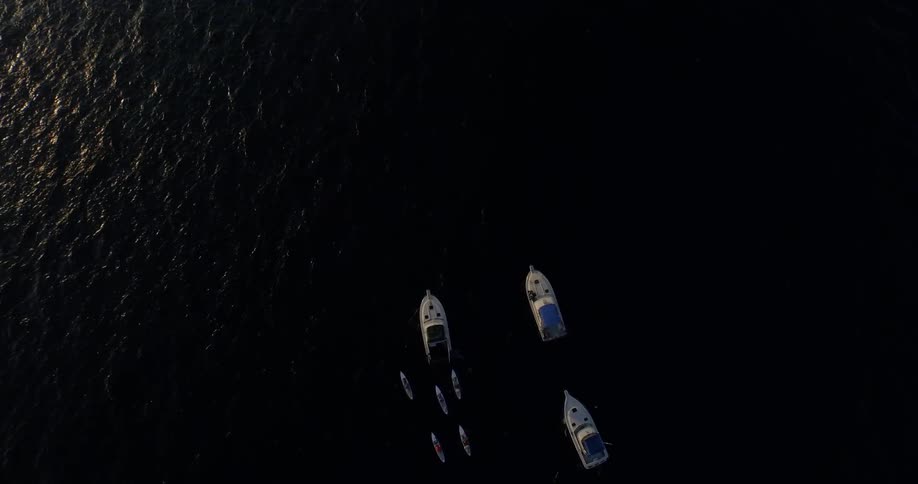Five people paddle boarding next to three boats in the middle of the ocean