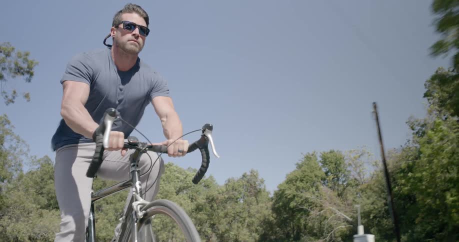 Muscular man wearing sunglasses rides a bike in the countryside