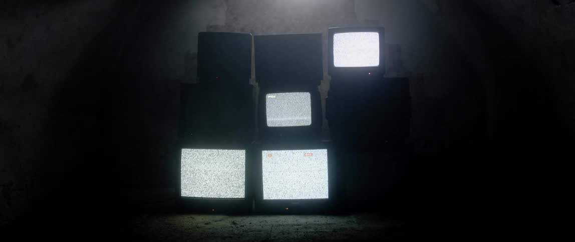 Nine old crt tvs sit stacked in rows of three in the darkness until they begin to power on displaying static