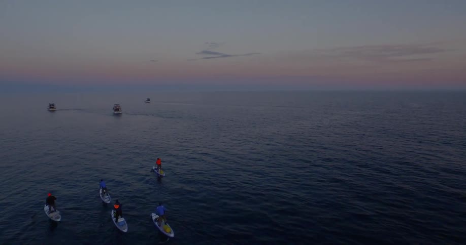 Paddle boarders and boats heading out to sea during sunset