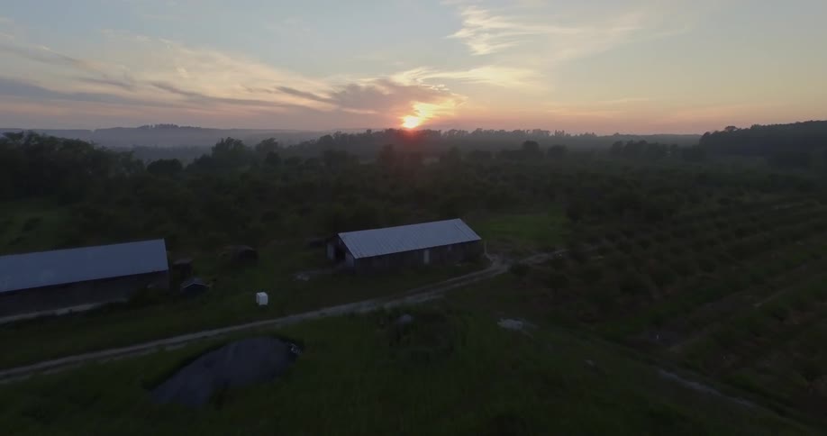 A the sun sits very low in the sky a farm can be seen amidst sprawling forests and fields
