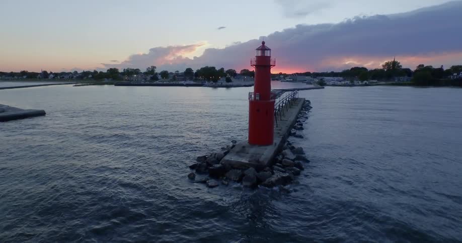 A small red lighthouse sits underneath a beautiful sunset on the ocean