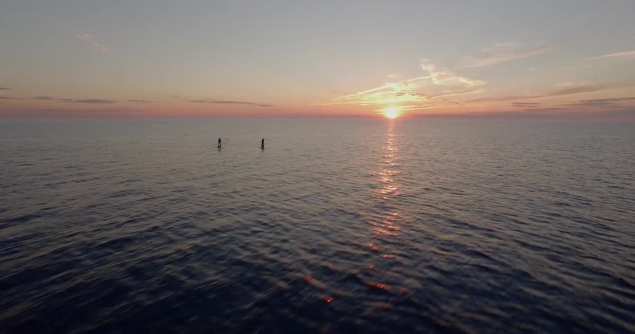 People on paddle boards in the ocean with the sunset in the background
