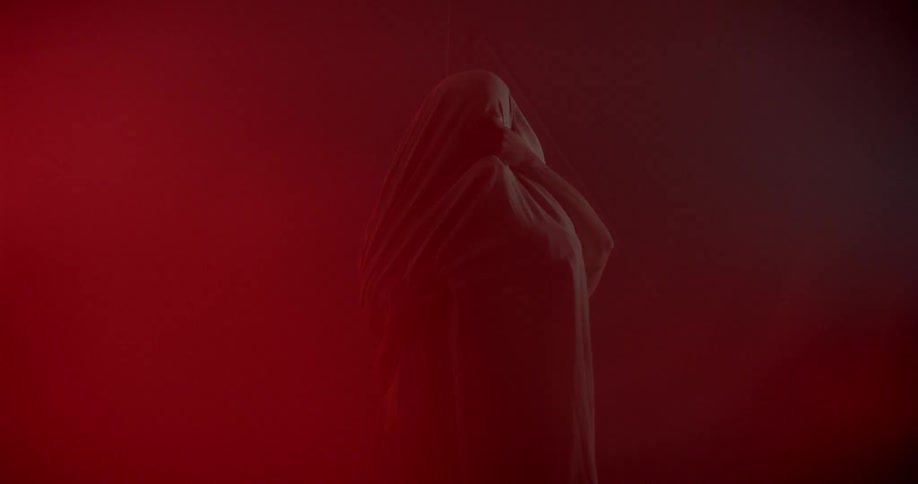 A couple appears to be hugging and kissing in a dark smoky room while one person is covered in a sheet