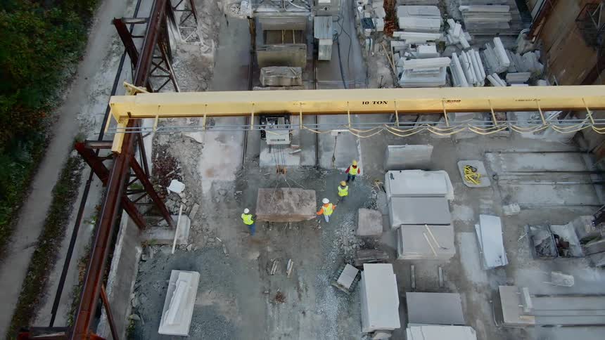 Construction workers walk beside a large object and machine