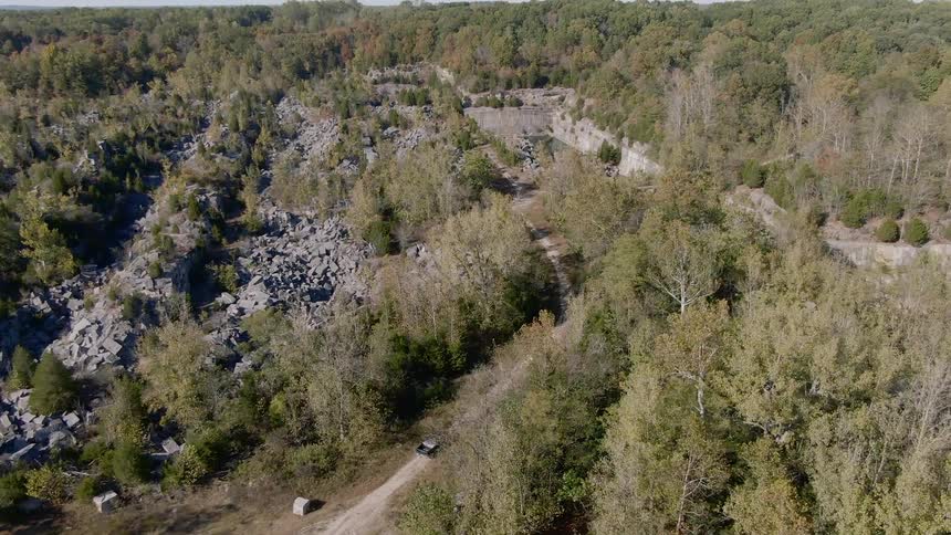 A car drives down a road past trees and piles of rock debris
