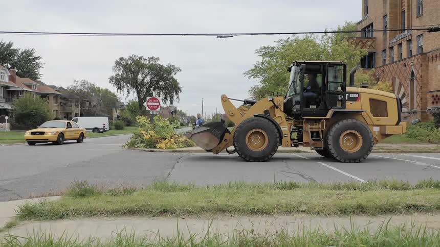 A bulldozer drives through a neighborhood and stops at an intersection
