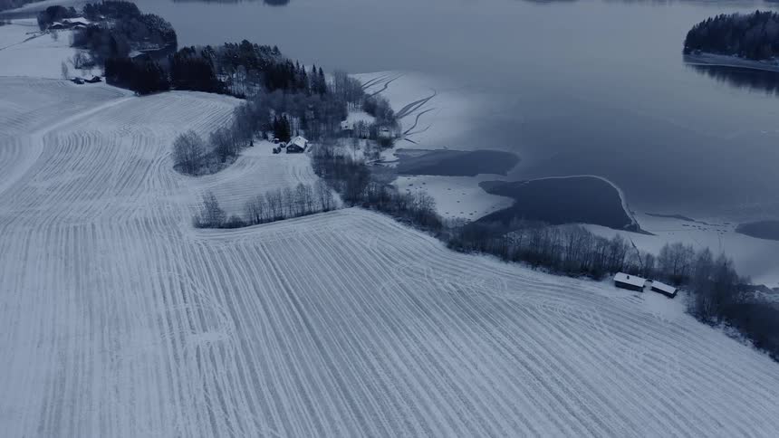 Farm buildings sit by snowy farmland and a lake