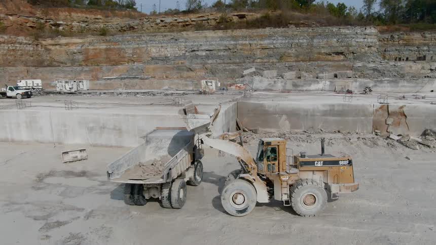 A bulldozer dumps rocks into the back of a dump truck