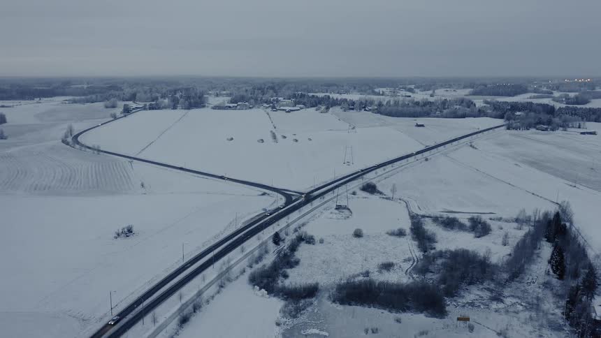 Cars driving down a highway surrounded by snow covered fields