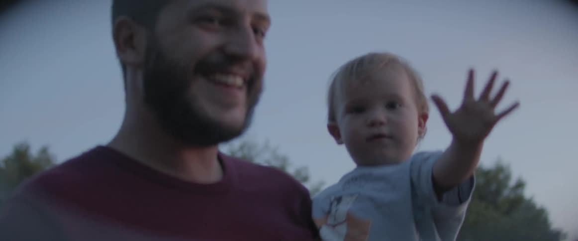A man holding a baby outdoors at dusk