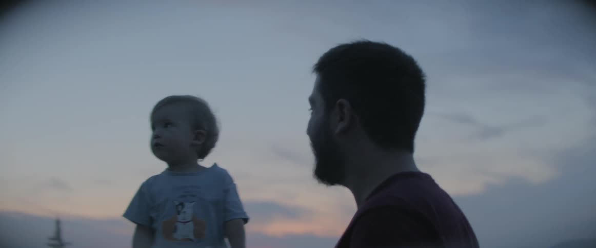 A man holding a babys hand and smiling as the baby points to the sky