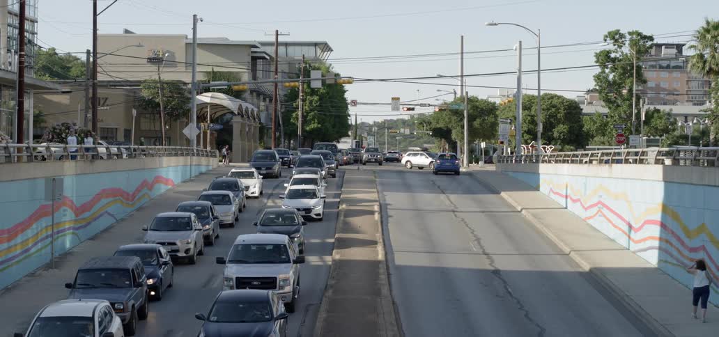 Cars driving down a city street and people walking on the sidewalk