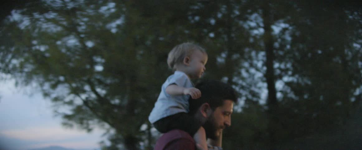 A man carries a toddler on his shoulders walking a trail